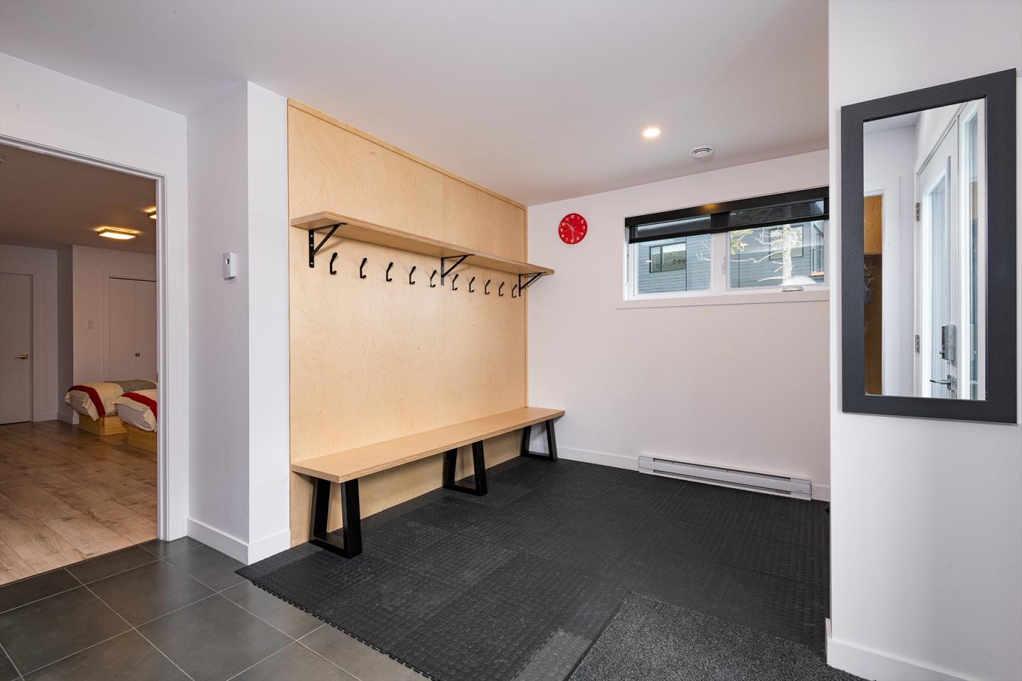 Vestiaire moderne avec banc et crochets muraux, sol noir et mur en bois clair.