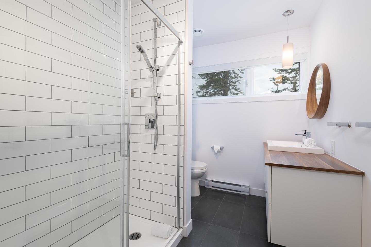 Salle de bain moderne avec douche en verre, miroir rond, lavabo sur meuble blanc.