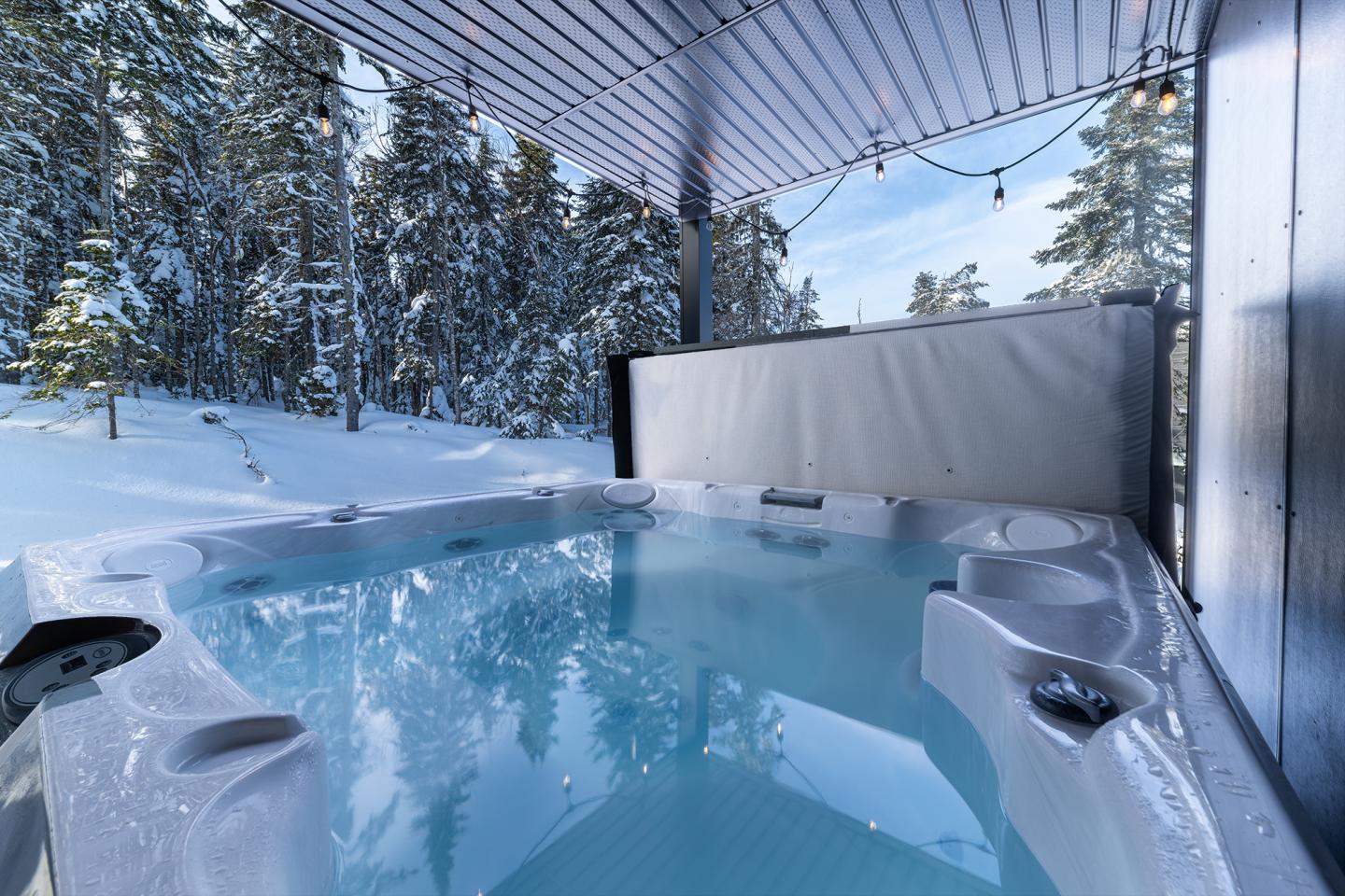 Spa extérieur entouré de neige sous un auvent.