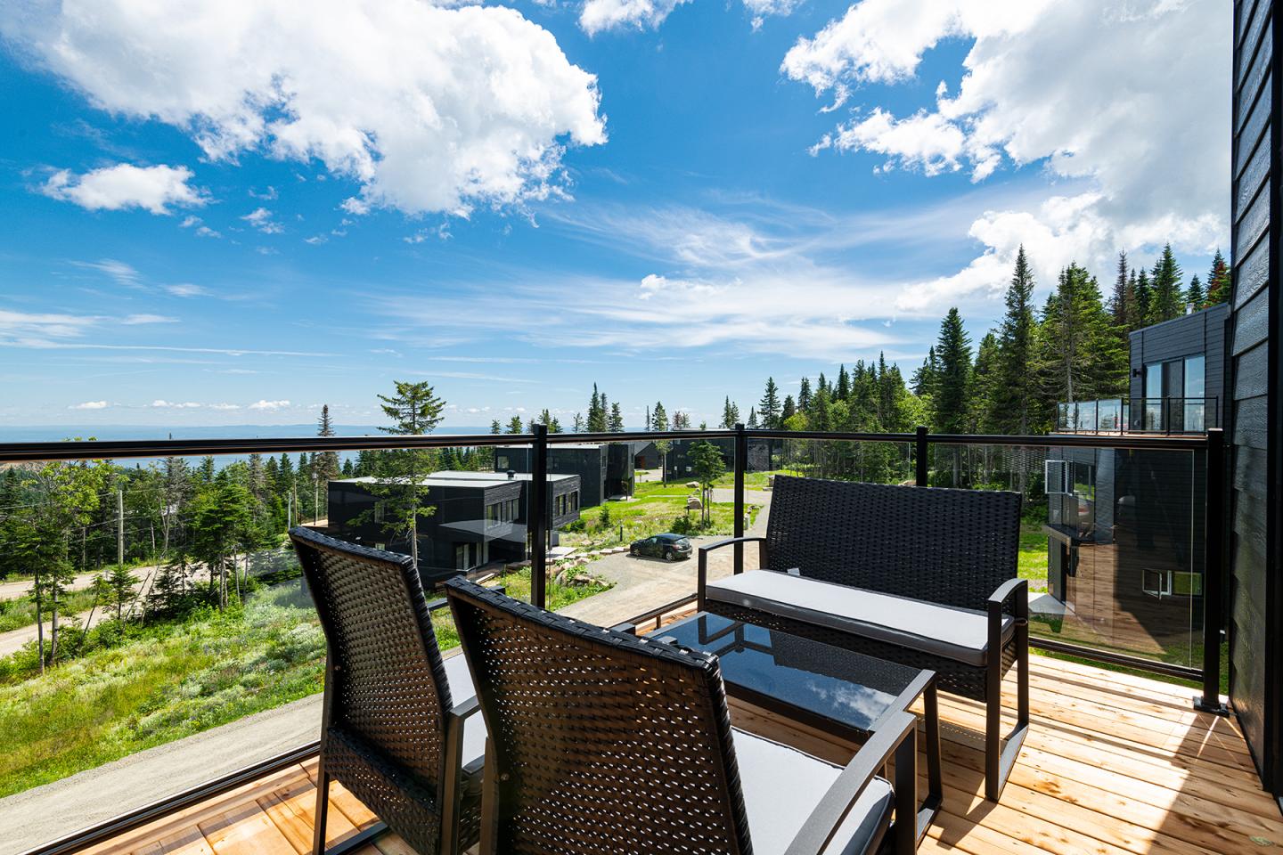 Terrasse ensoleillée avec vue sur la forêt et le ciel bleu, chaises et table en bois.