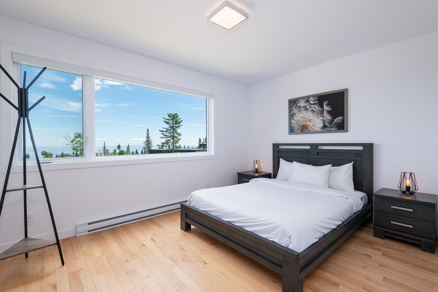 Chambre lumineuse avec lit double, fenêtre vue mer et arbres.