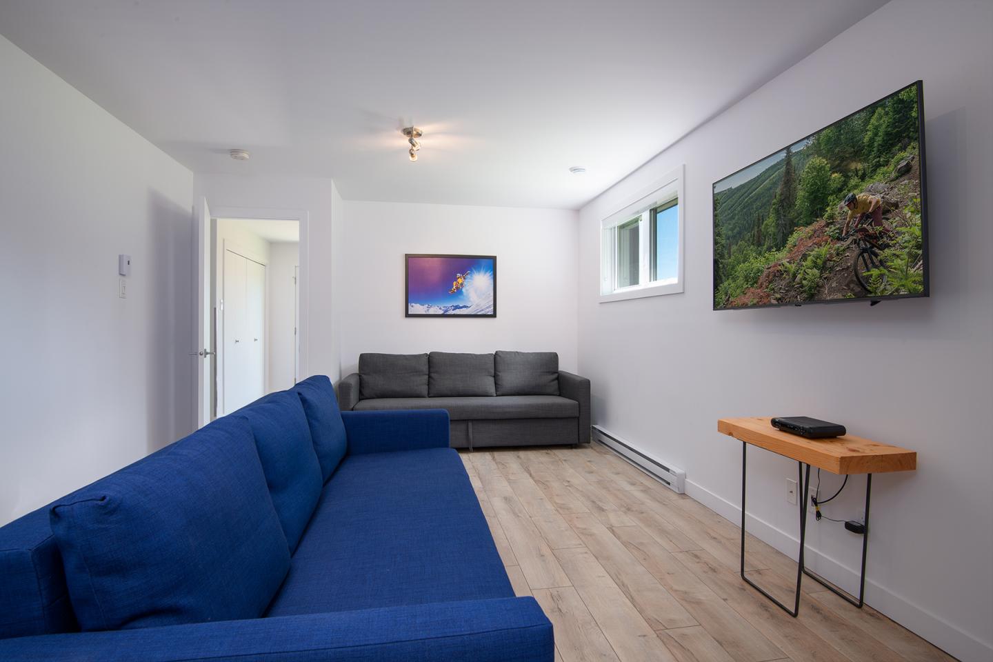 Salon moderne avec deux canapés, TV murale et table basse en bois.