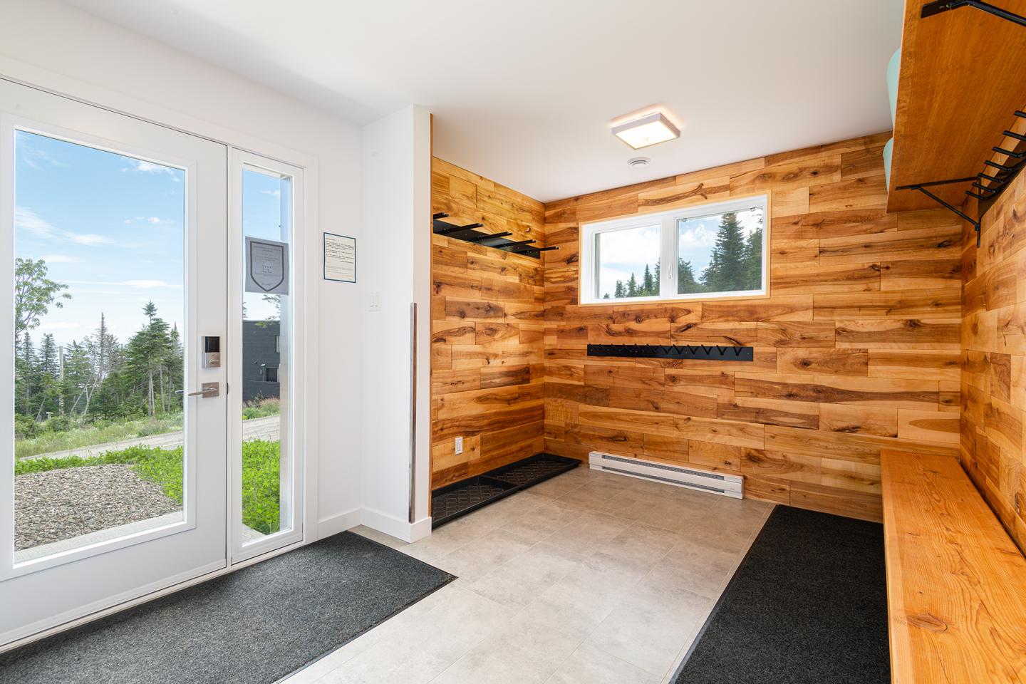 Intérieur lumineux en bois avec bancs noirs, porte-fenêtre donnant sur jardin.