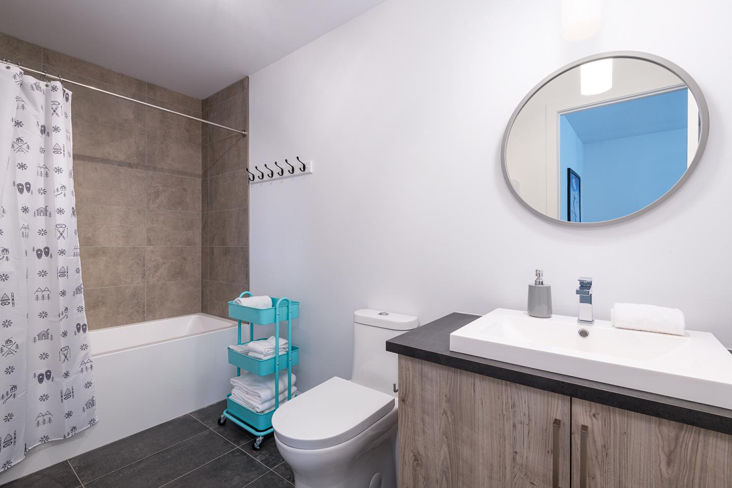 Salle de bain moderne avec baignoire, miroir rond, et étagère turquoise.