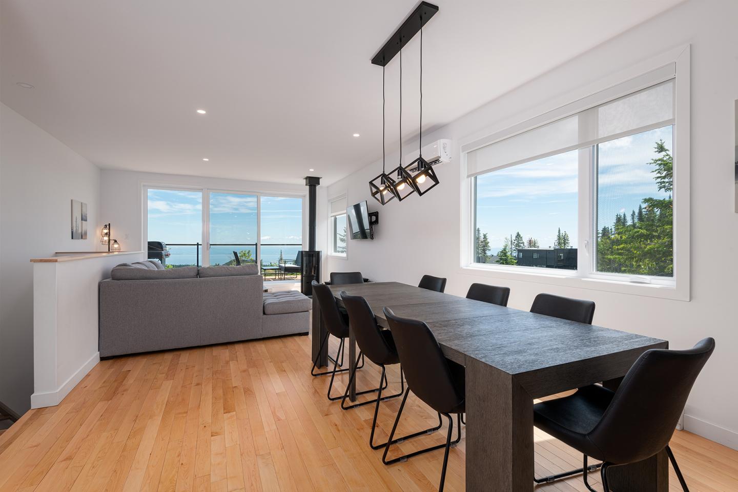 Salle à manger moderne avec table noire, chaises noires et grandes fenêtres.