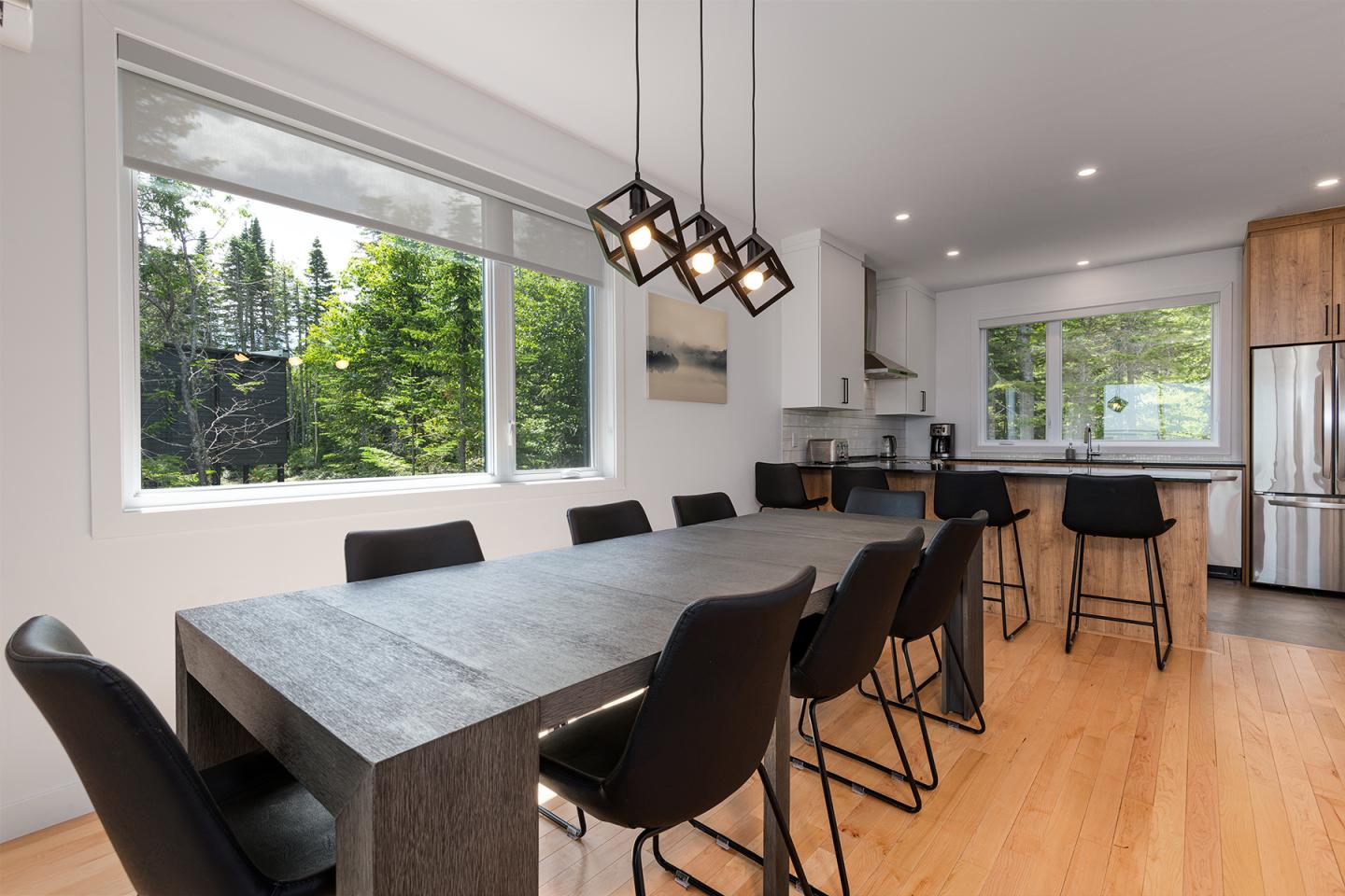 Salle à manger moderne avec table noire et chaises, vue sur jardin.