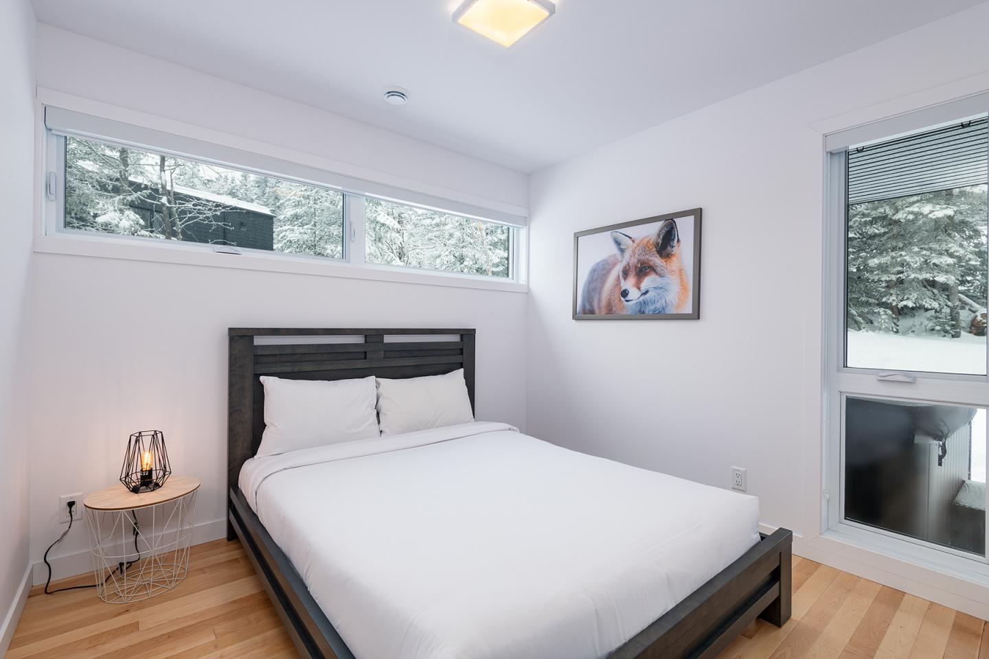 Chambre lumineuse avec un lit double, vue sur des arbres enneigés.