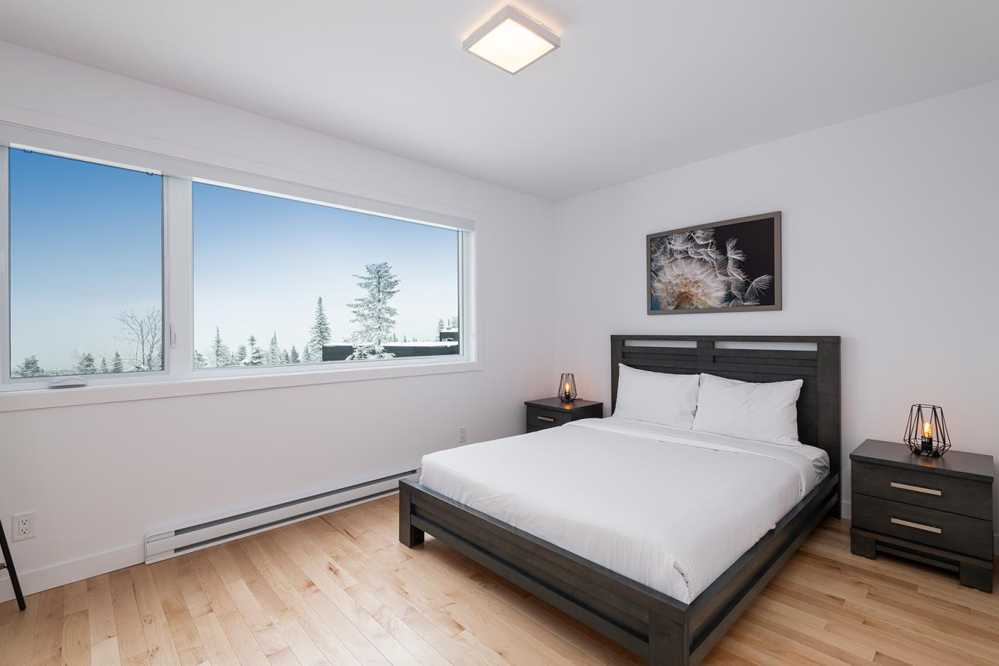 Chambre lumineuse avec lit double, fenêtre sur paysage enneigé.