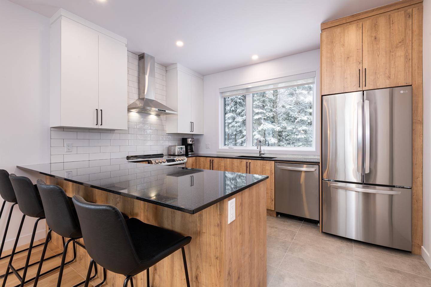 Cuisine moderne avec îlot central en bois, comptoir en granit noir, et électroménagers en acier inoxydable.