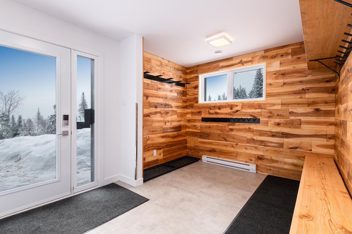 Vestiaire en bois avec fenêtre et porte donnant sur la neige.