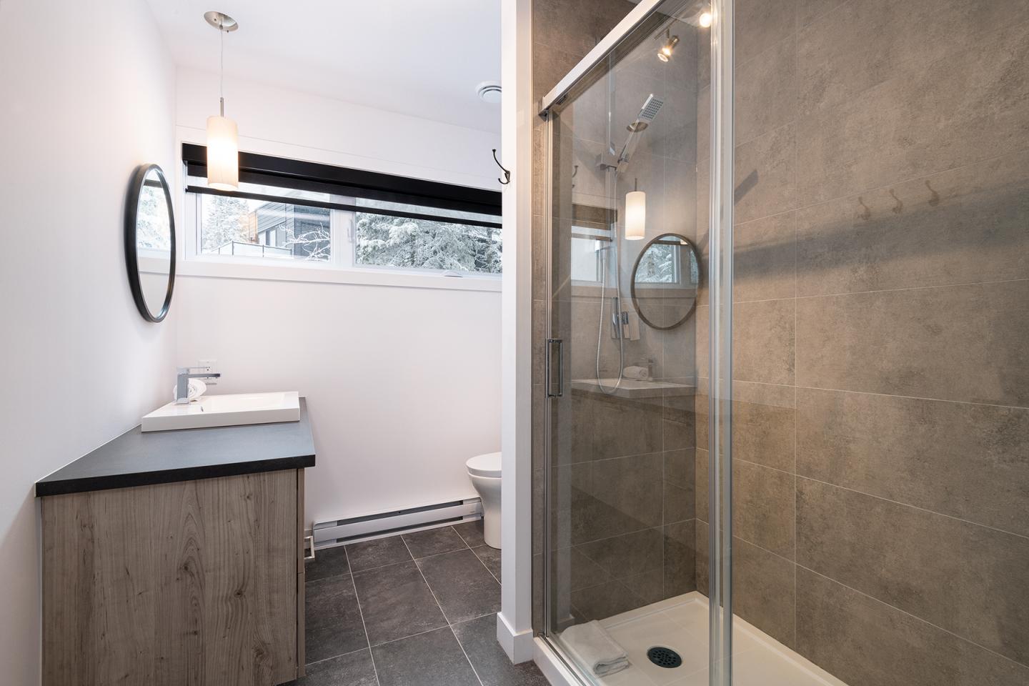 Salle de bain moderne avec douche vitrée et lavabo, murs blancs.