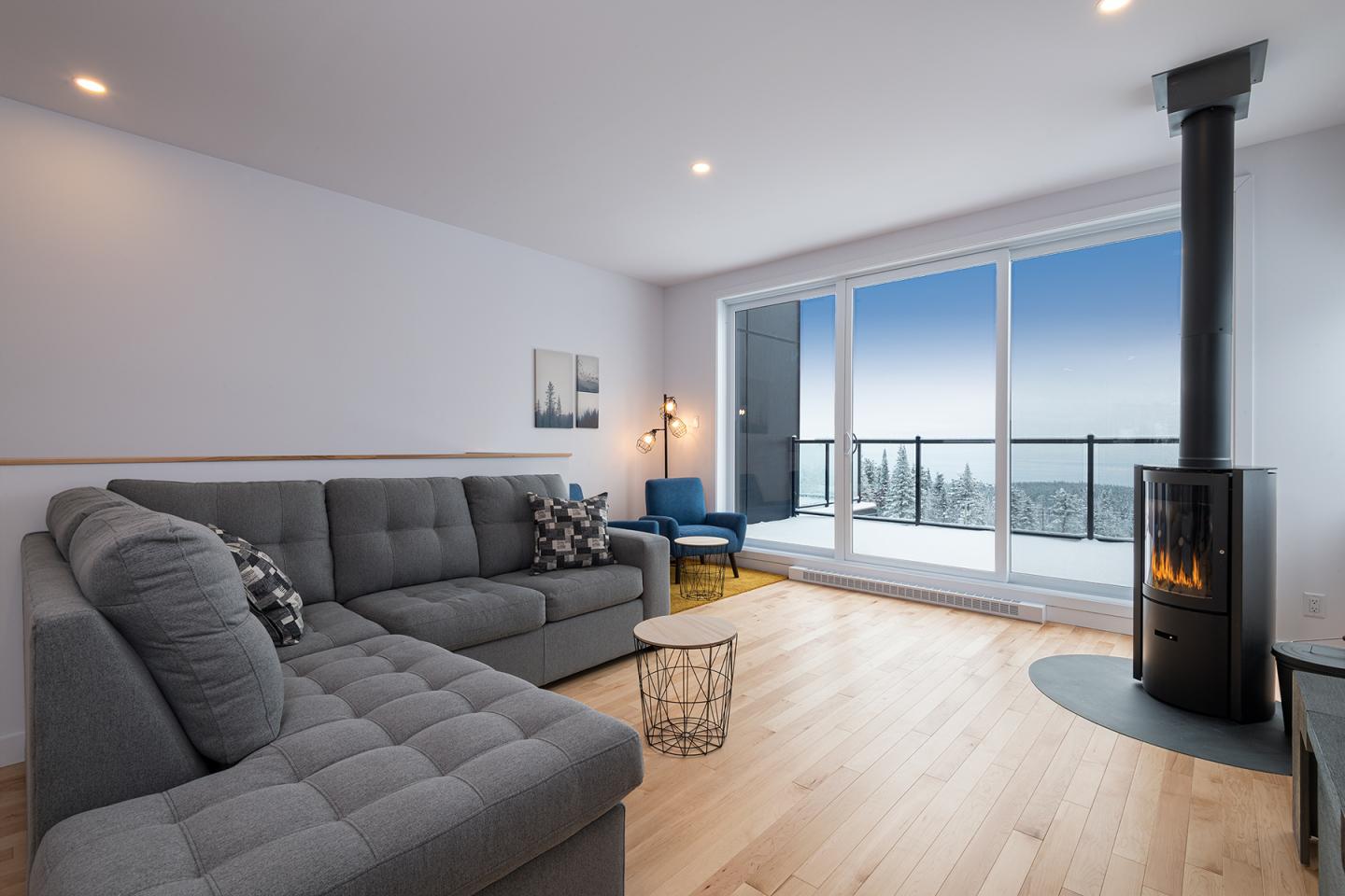 Salon moderne avec canapé gris, cheminée et grandes fenêtres avec vue sur la mer.