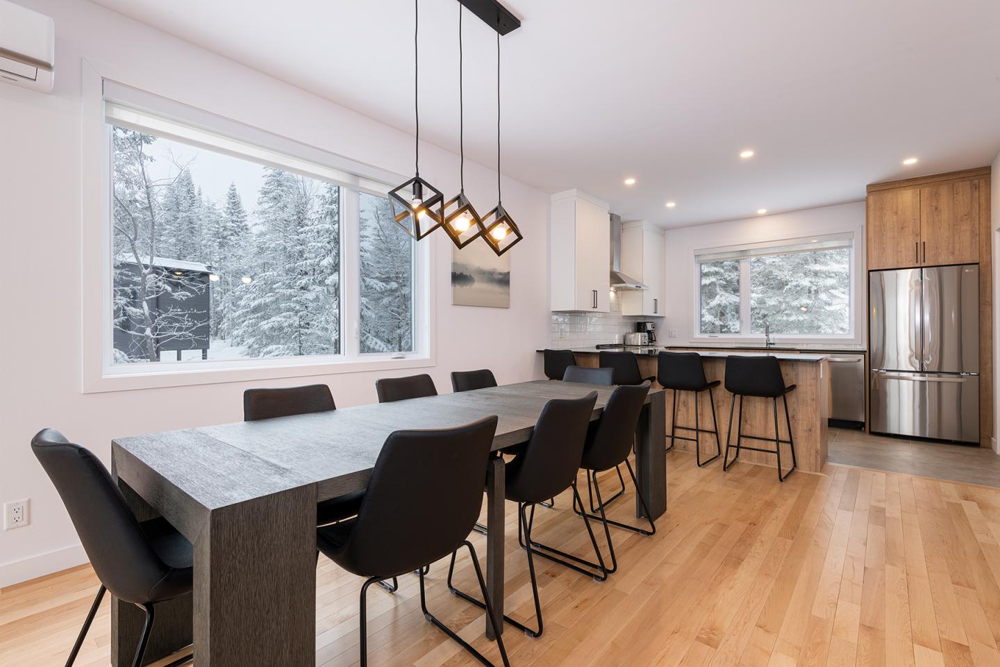 Salle à manger moderne avec table noire, chaises, fenêtres avec vue sur la neige.