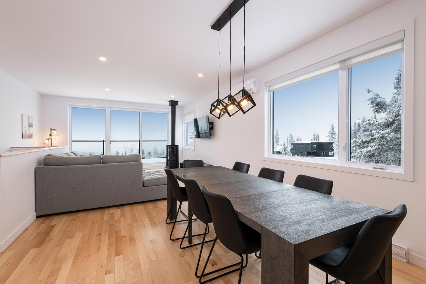 Salle à manger moderne avec table en bois, chaises noires, vue sur la neige par la fenêtre.