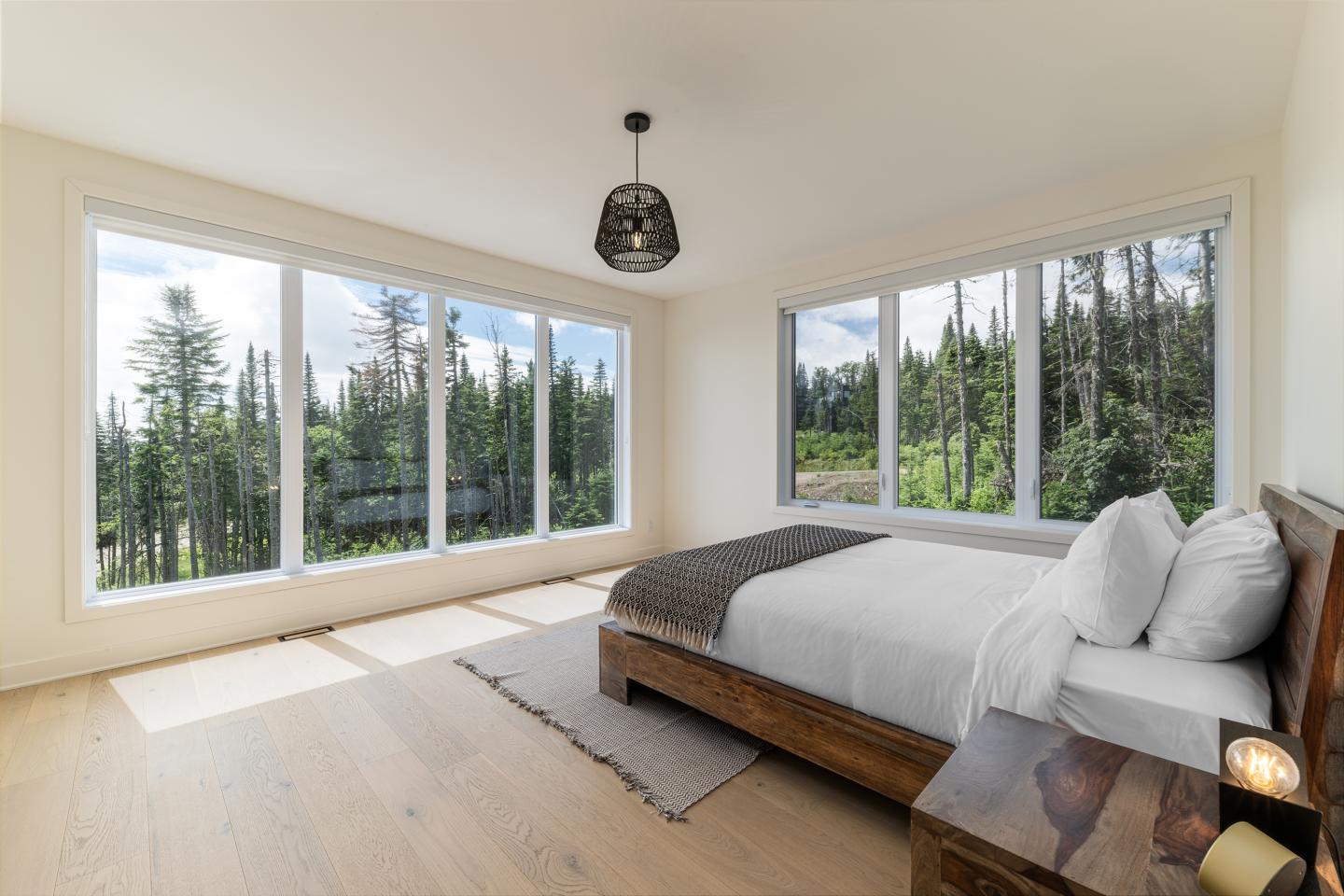 Chambre moderne avec lit double, grandes fenêtres donnant sur la forêt.