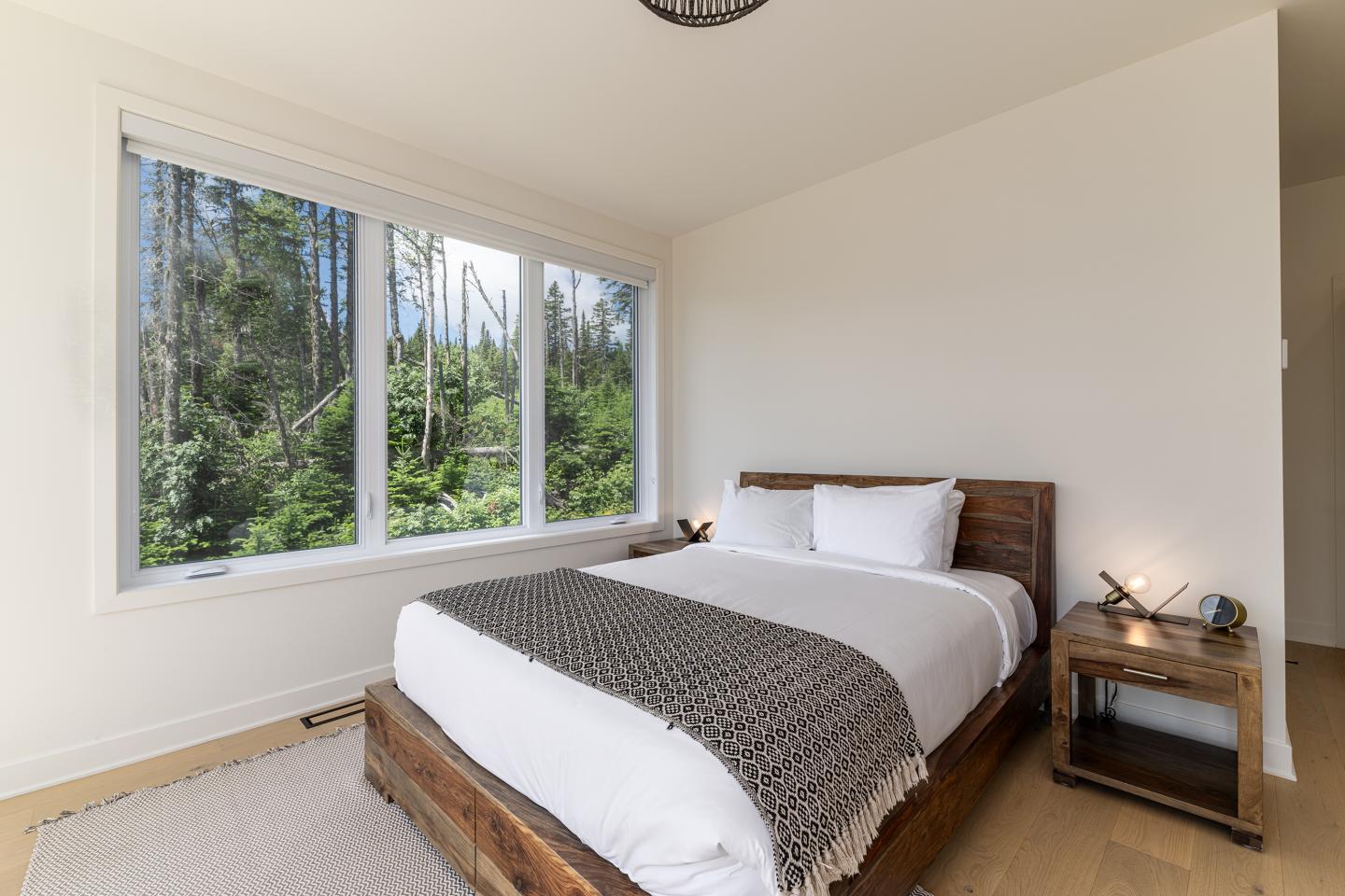 Chambre moderne avec lit double, grande fenêtre donnant sur la forêt.