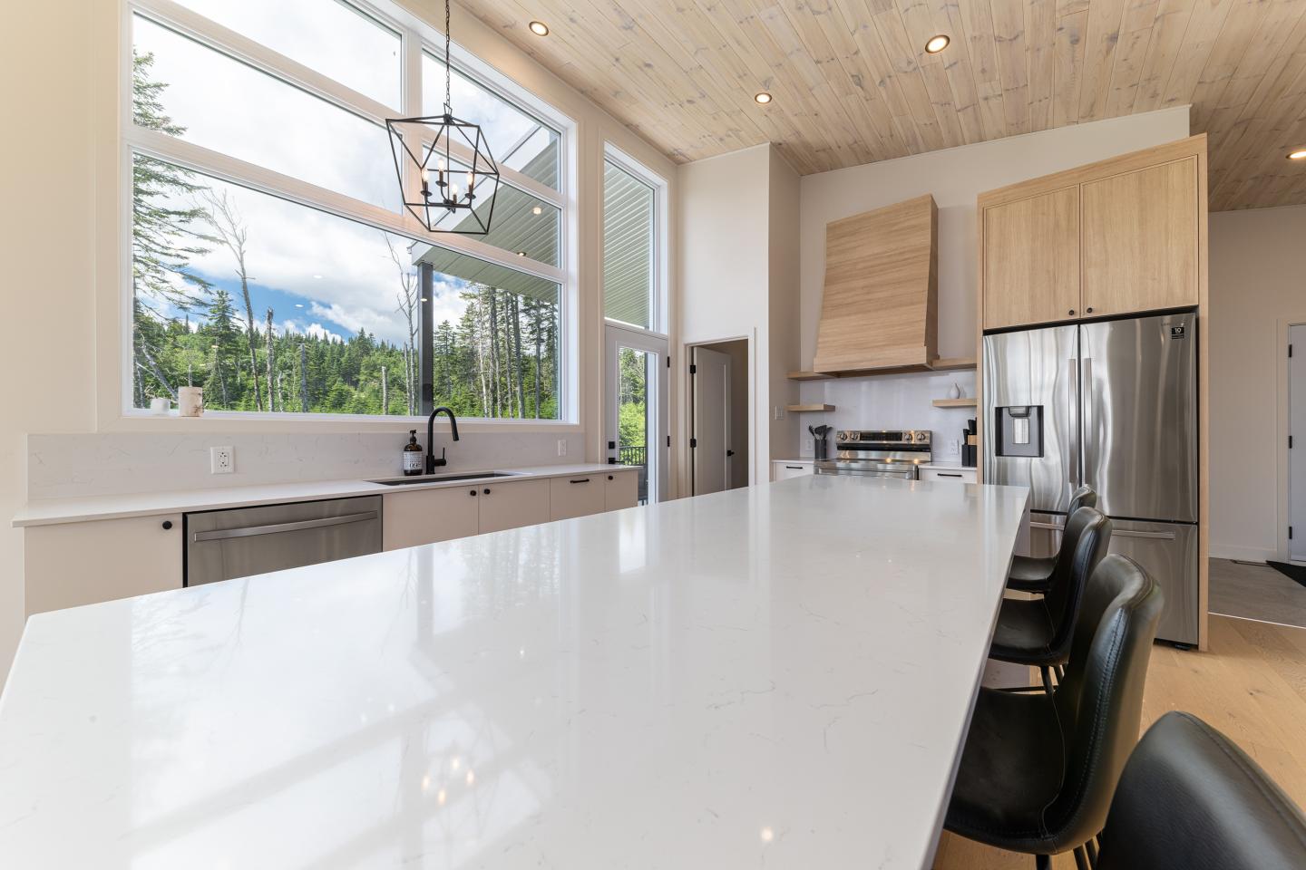 Cuisine moderne avec îlot central en marbre blanc, grandes fenêtres et électroménagers en inox.