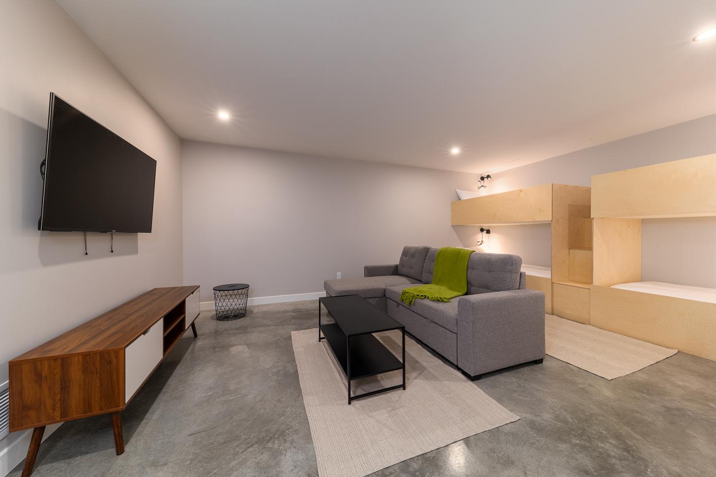 Salon minimaliste avec canapé gris, couverture verte, télé murale et meubles en bois.