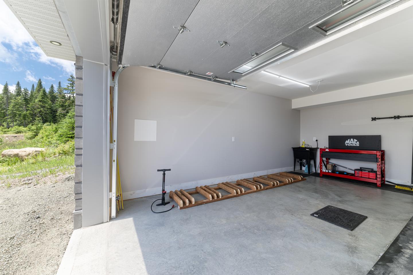 Garage ouvert, vide, avec établi rouge et pompe à vélo. Forêt visible dehors.