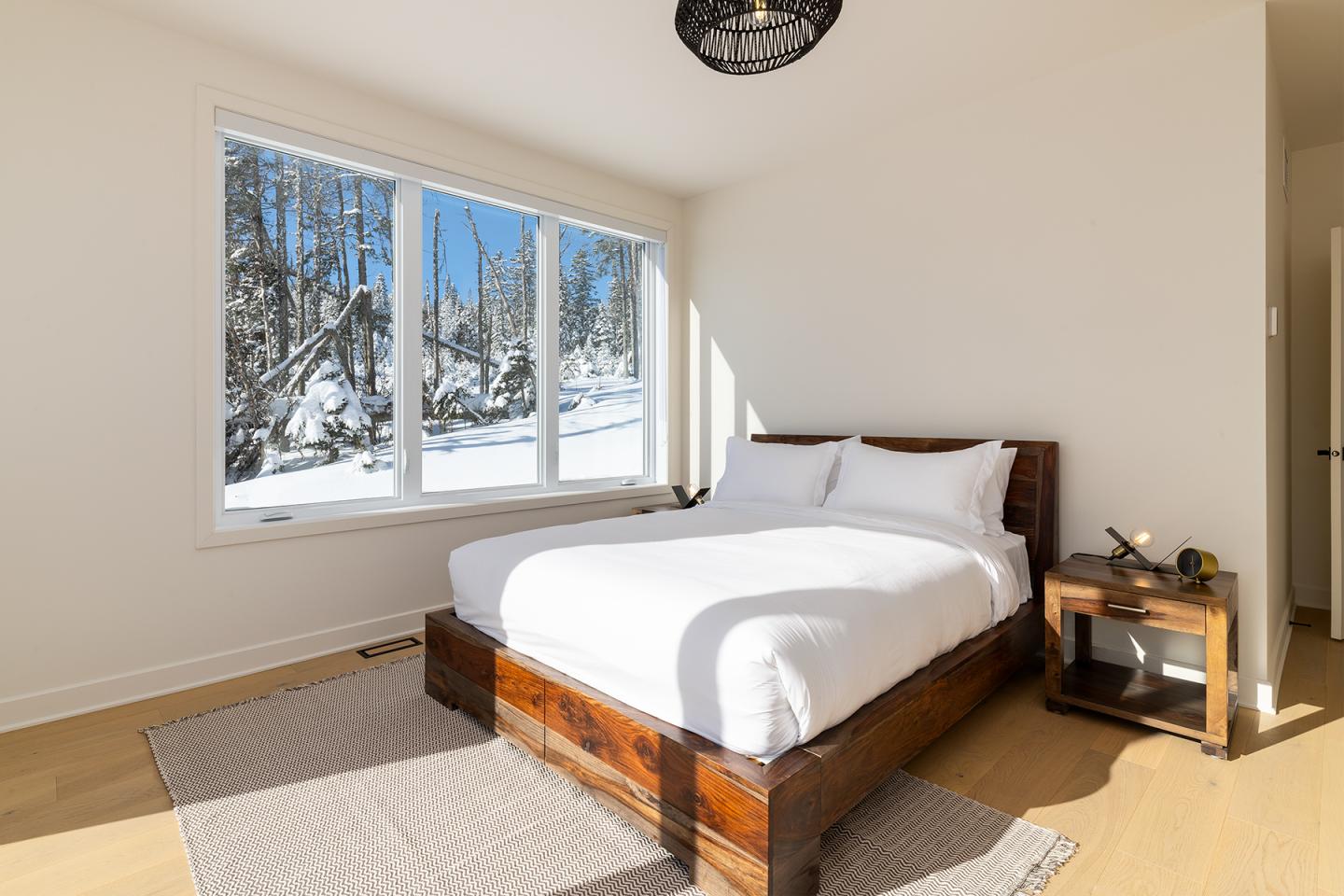 Chambre lumineuse avec lit en bois, grande fenêtre vue sur neige.