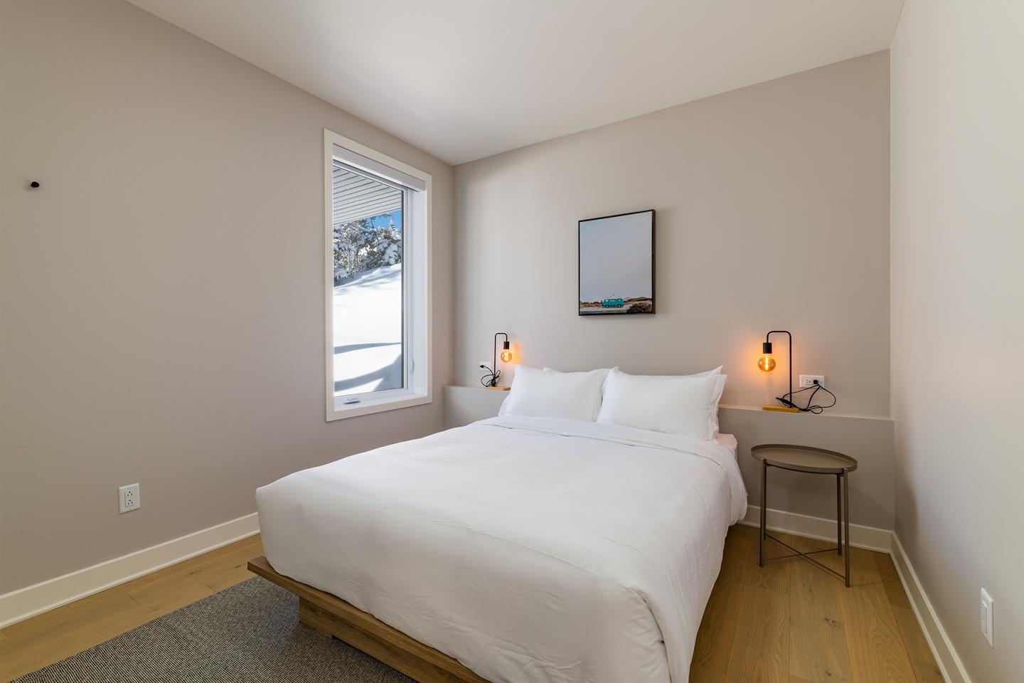 Chambre minimaliste avec lit double blanc, table de chevet et lampe.