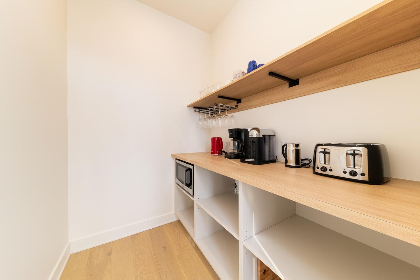 Petite cuisine avec étagères en bois, cafetière, grille-pain et micro-ondes.