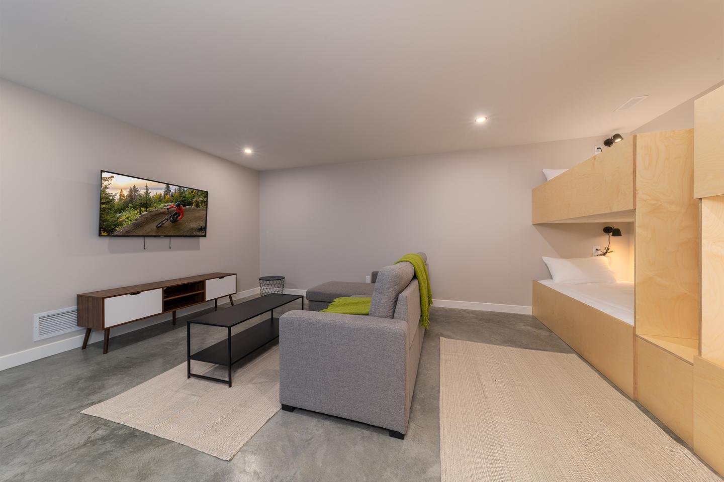 Salon moderne avec canapé gris, télé, et lits superposés en bois clair.