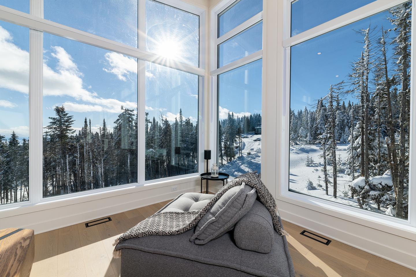 Salon lumineux avec vue sur forêt enneigée, ciel bleu et soleil brillant.