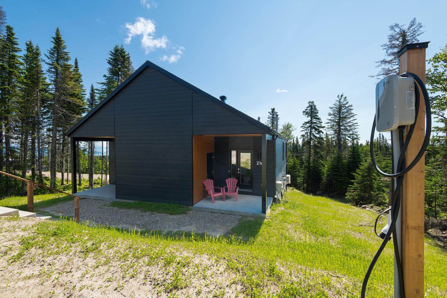 Chalet noir moderne entouré de forêts et de ciel bleu clair.