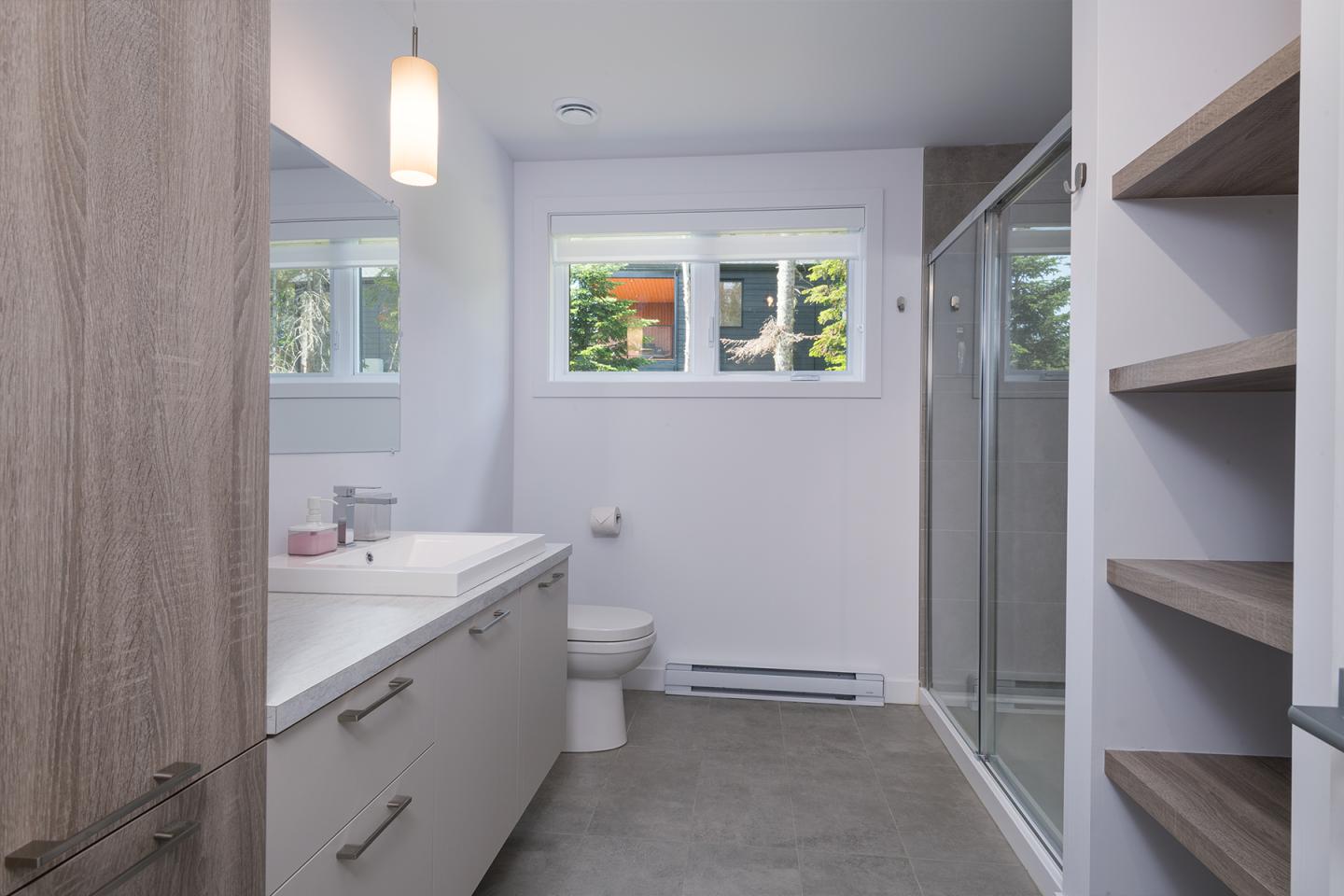 Salle de bain moderne avec douche vitrée, lavabo et étagères en bois.