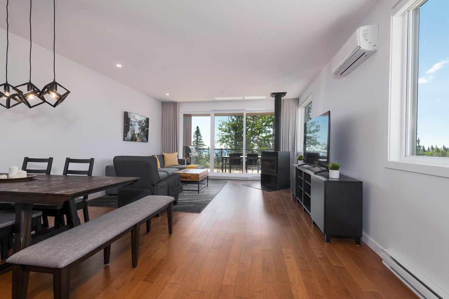 Salon moderne avec parquet, mobilier noir, vue sur balcon et arbres verdoyants.