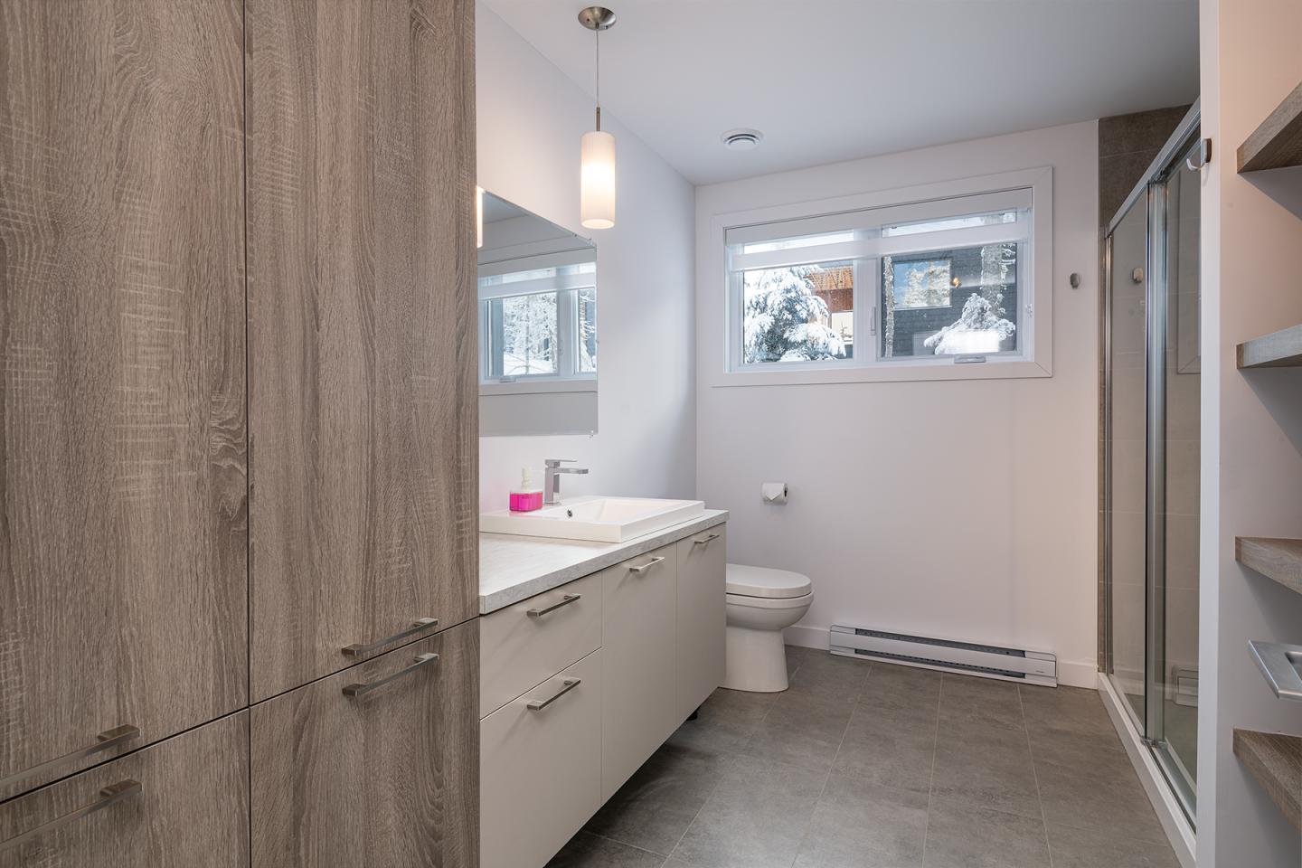 Salle de bain moderne avec douche, lavabo, toilette et fenêtre lumineuse.