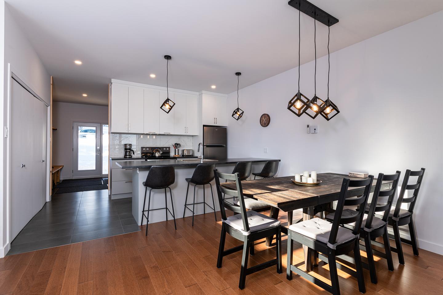 Salle à manger moderne avec table noire, chaises, et suspensions lumineuses.