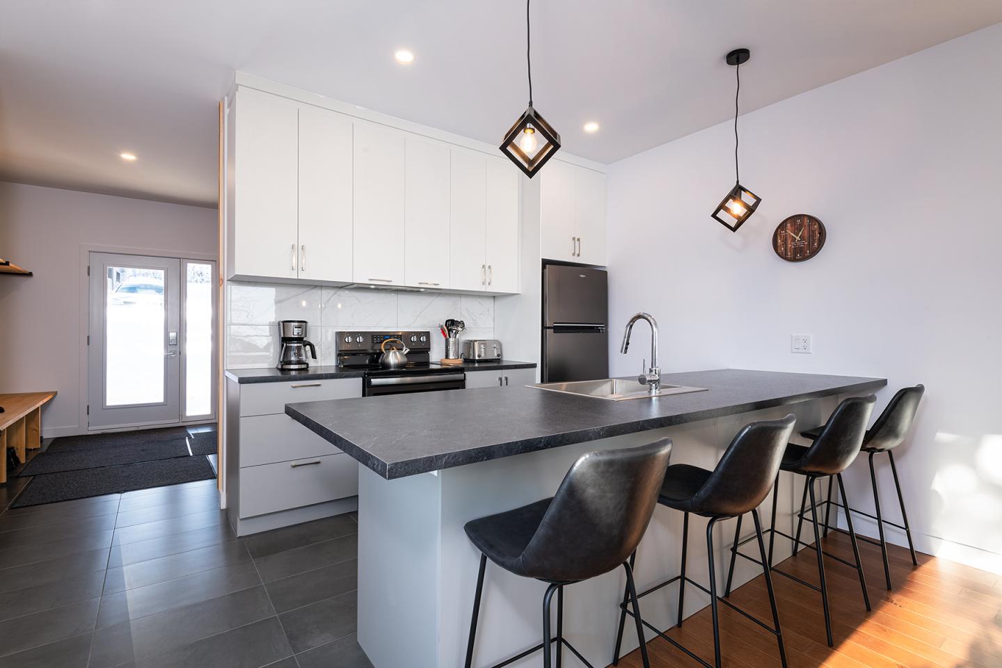 Cuisine moderne avec un îlot central, chaises noires, éclairage suspendu.