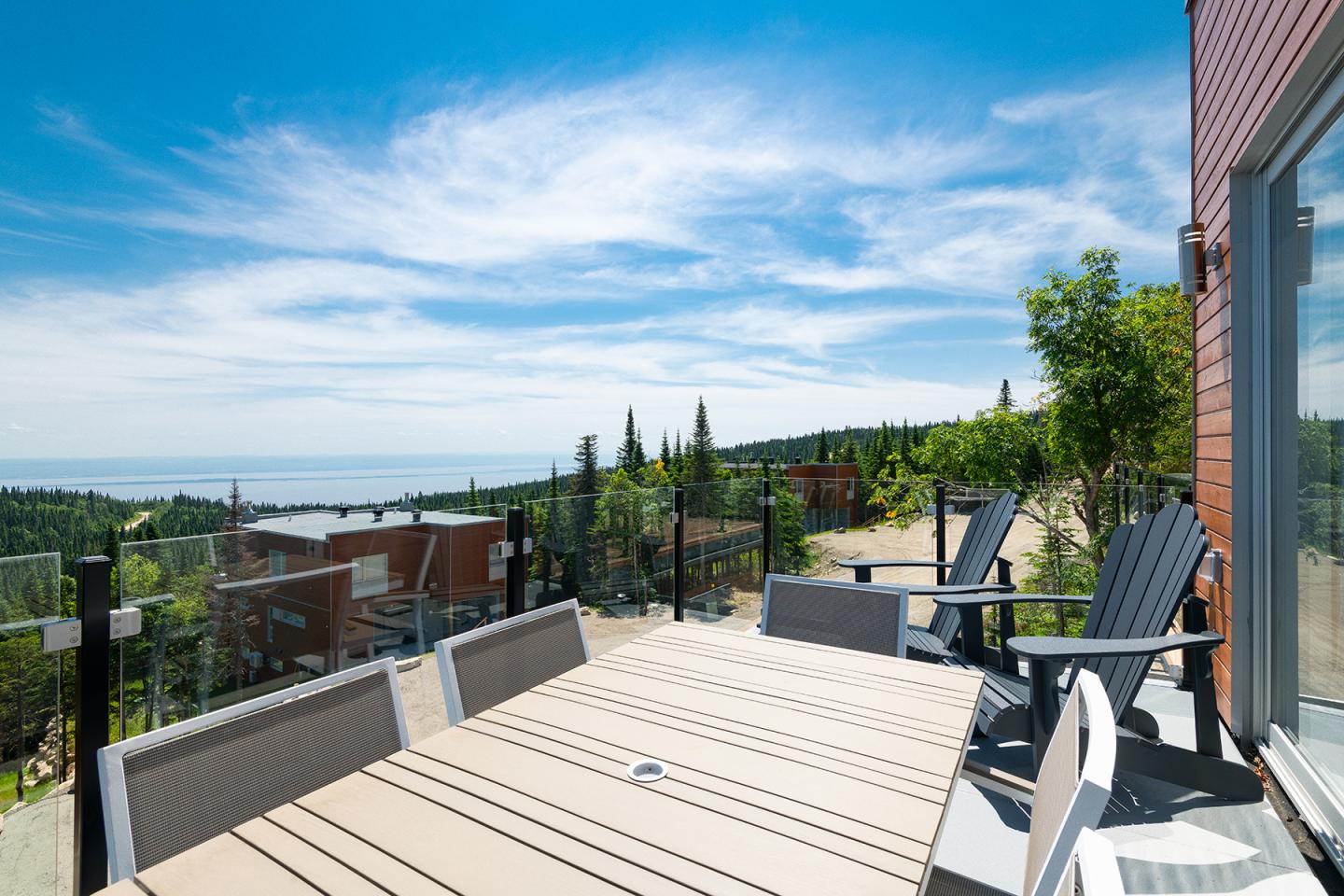 Terrasse ensoleillée avec vue sur la mer et chaises noires.