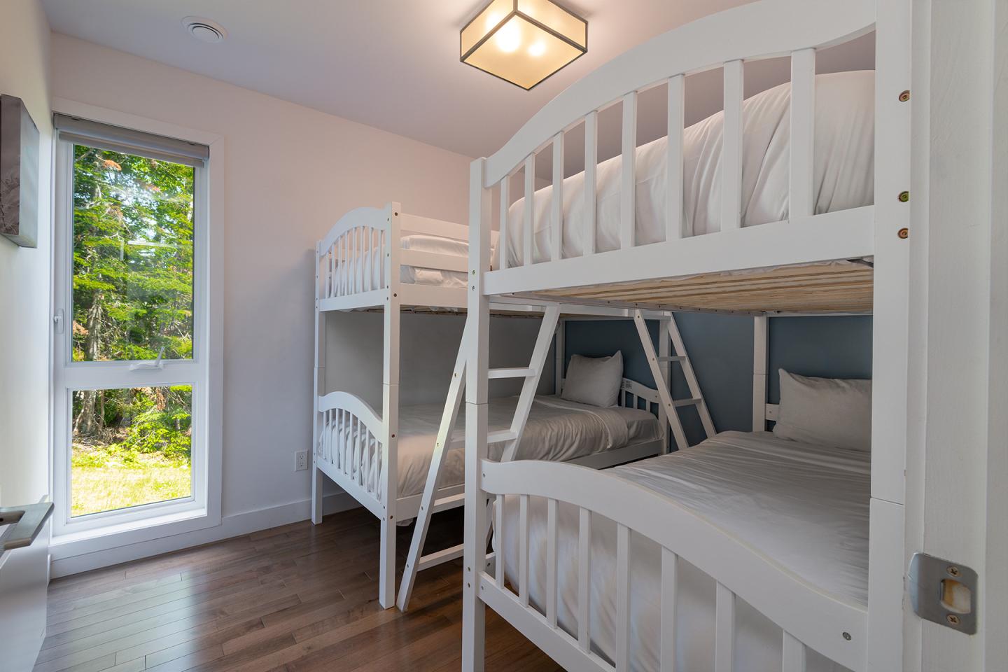 Chambre avec deux lits superposés blancs, fenêtre et parquet en bois.