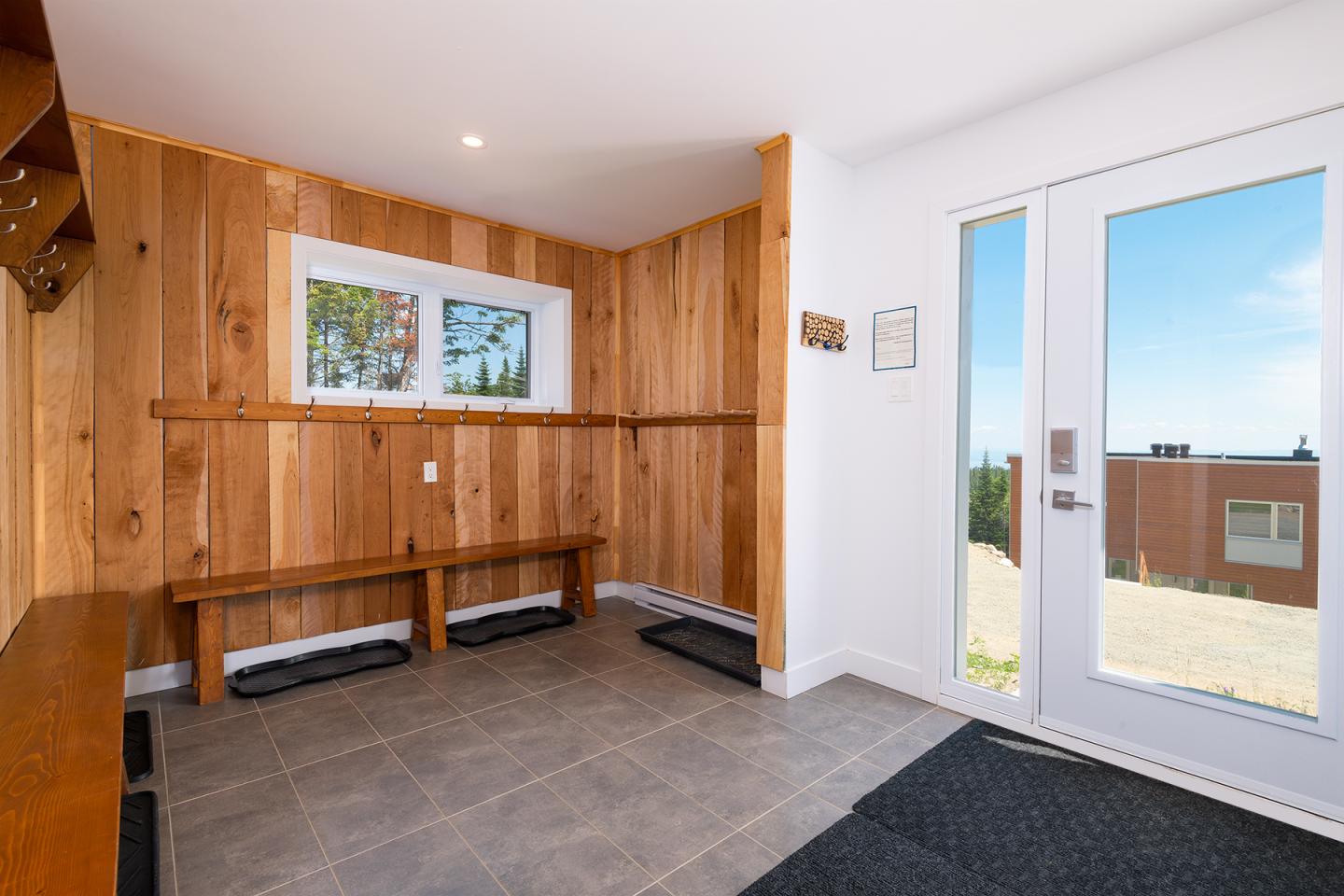 Entrée en bois clair avec bancs, fenêtre et porte vitrée donnant sur l'extérieur.