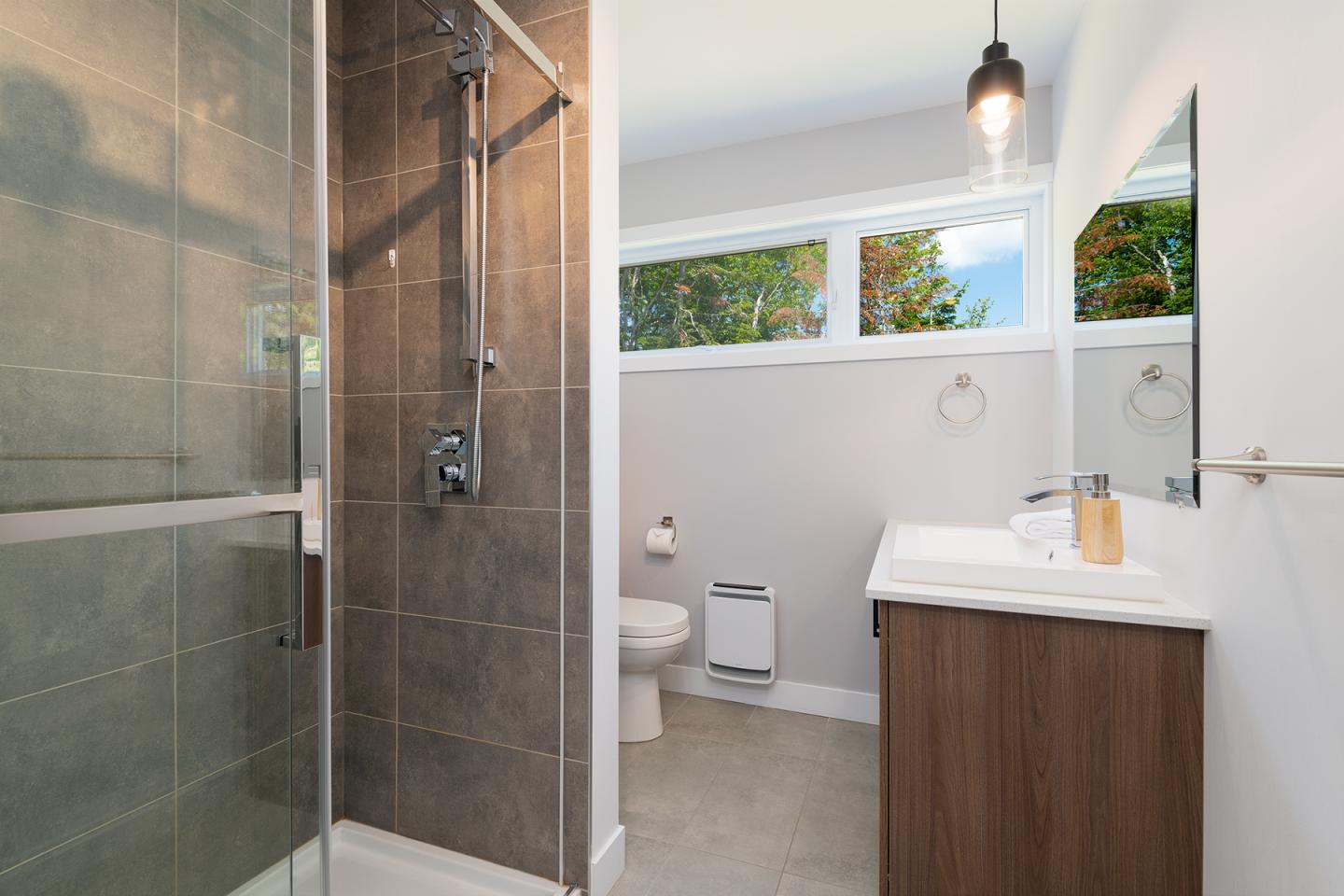 Salle de bain moderne avec douche vitrée, lavabo et toilettes, éclairée naturellement.