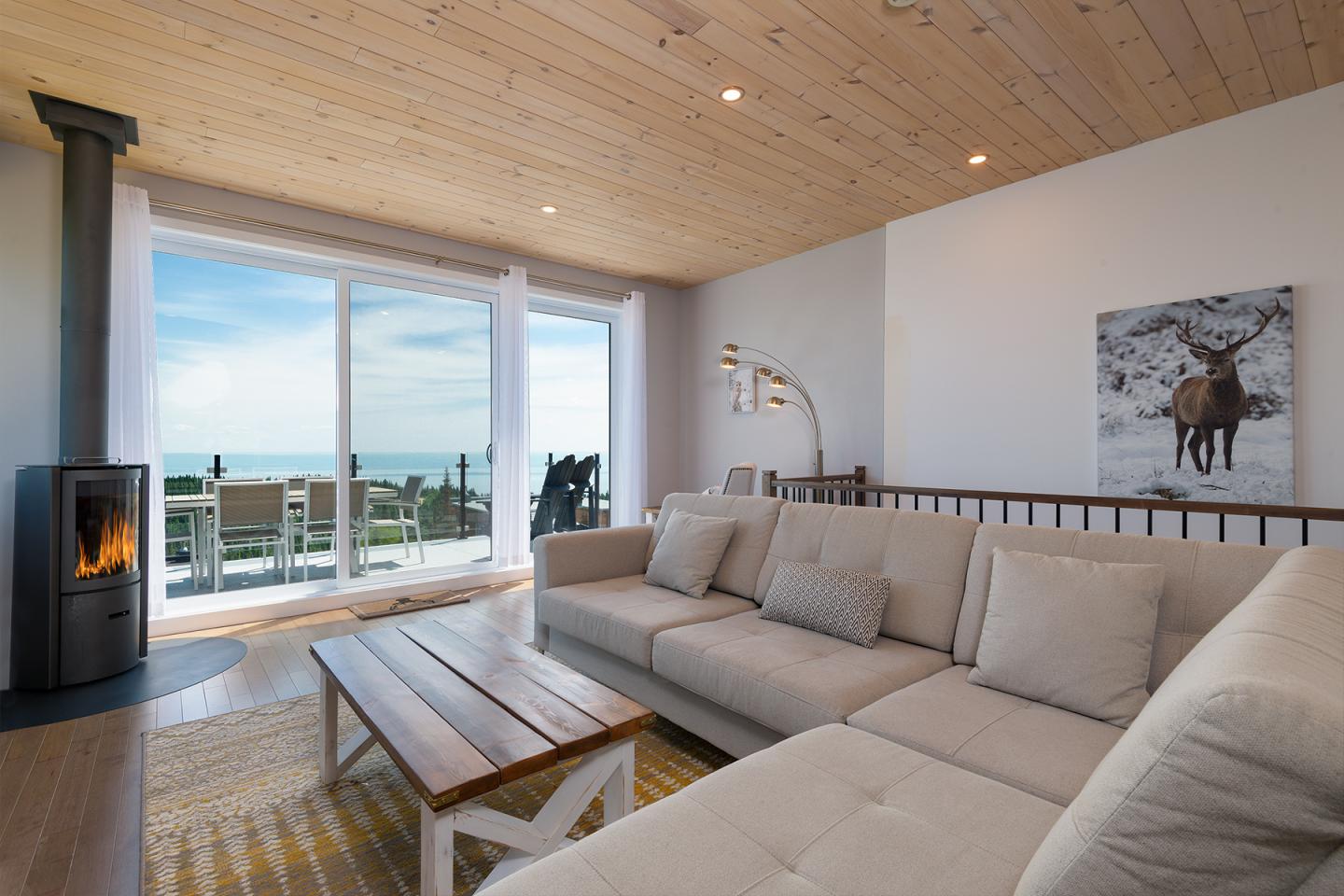 Salon lumineux, grand canapé beige, vue sur la mer par une baie vitrée.