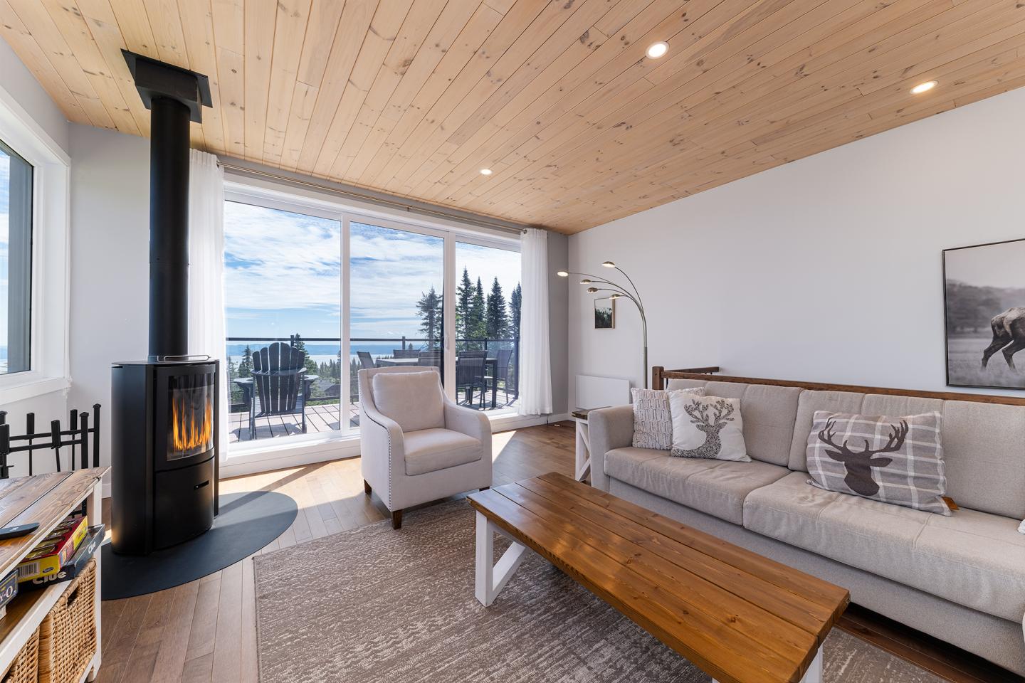 Salon moderne avec poêle à bois, canapé, et grandes fenêtres offrant vue sur la mer.