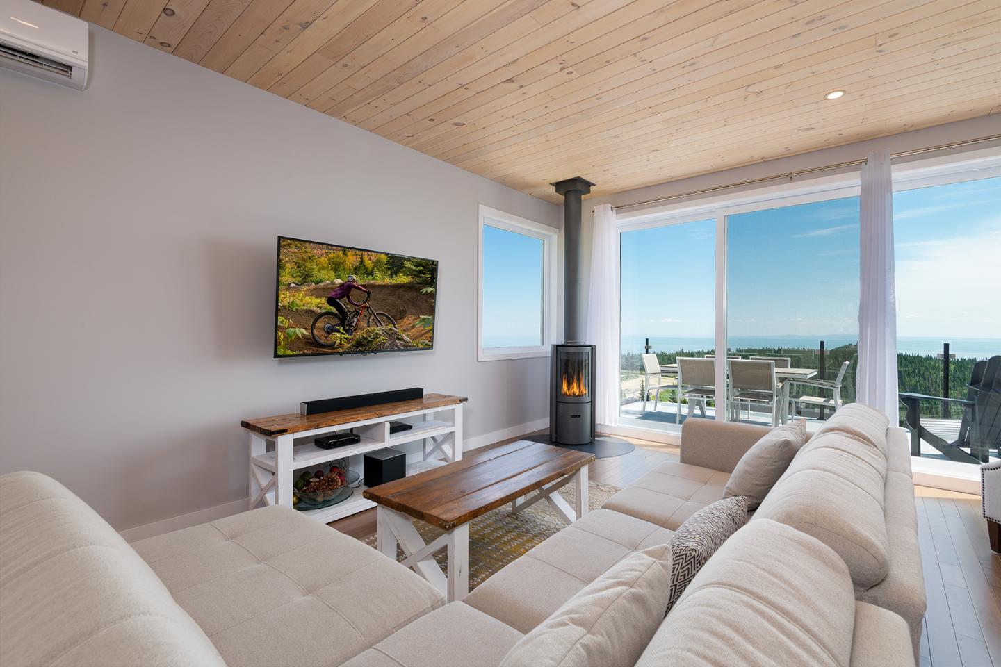 Salon moderne avec canapé blanc et cheminée, vue sur terrasse ensoleillée.