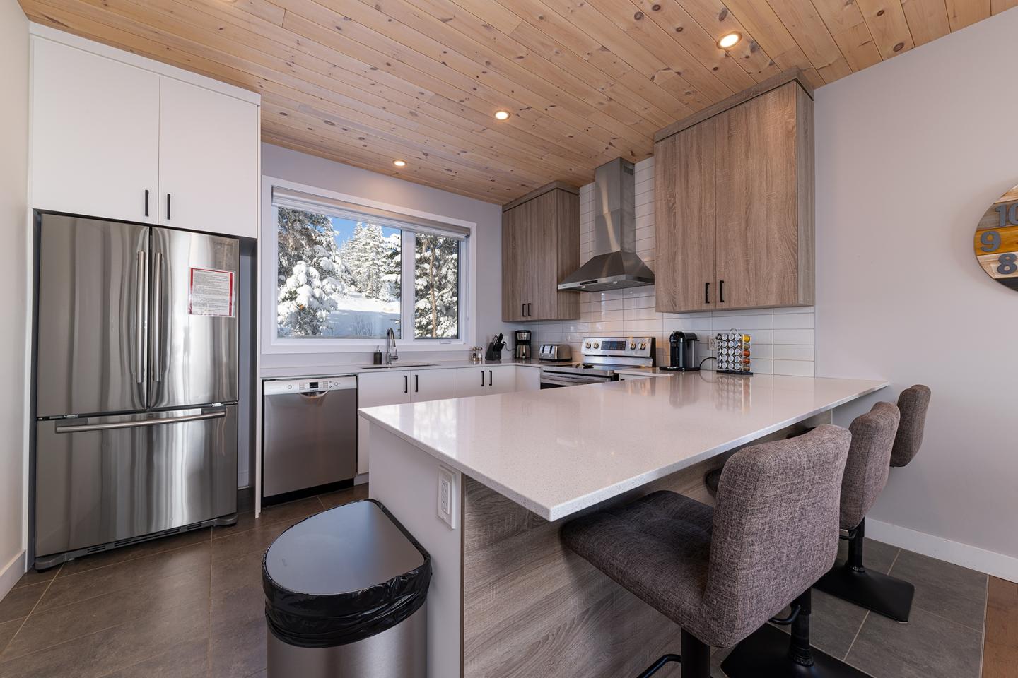 Cuisine moderne avec îlot, réfrigérateur en acier inoxydable et vue sur neige par la fenêtre.