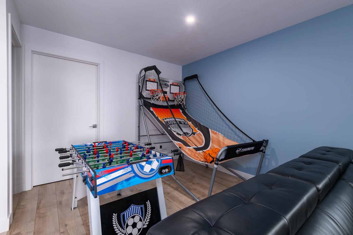 Salle de jeux avec baby-foot et jeu de basket sur sol en bois clair.