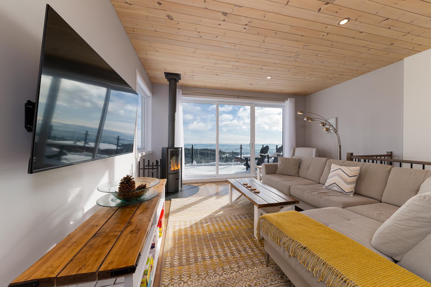 Salon moderne avec vue sur la mer, grandes fenêtres, canapé beige et cheminée.