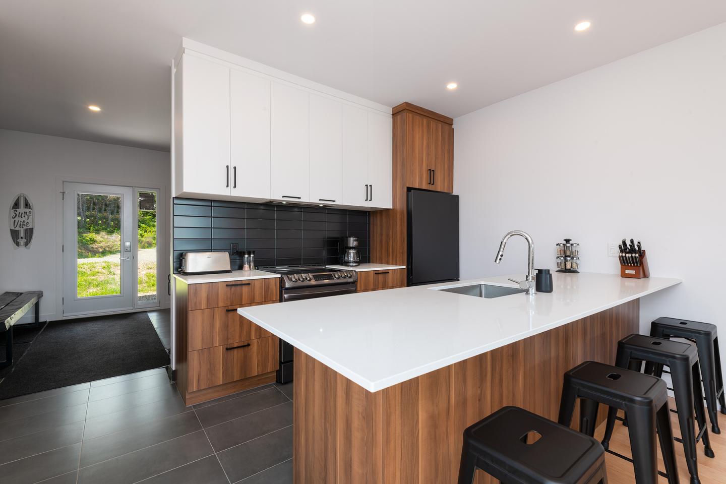 Cuisine moderne avec meubles en bois, plan de travail blanc et tabourets noirs.