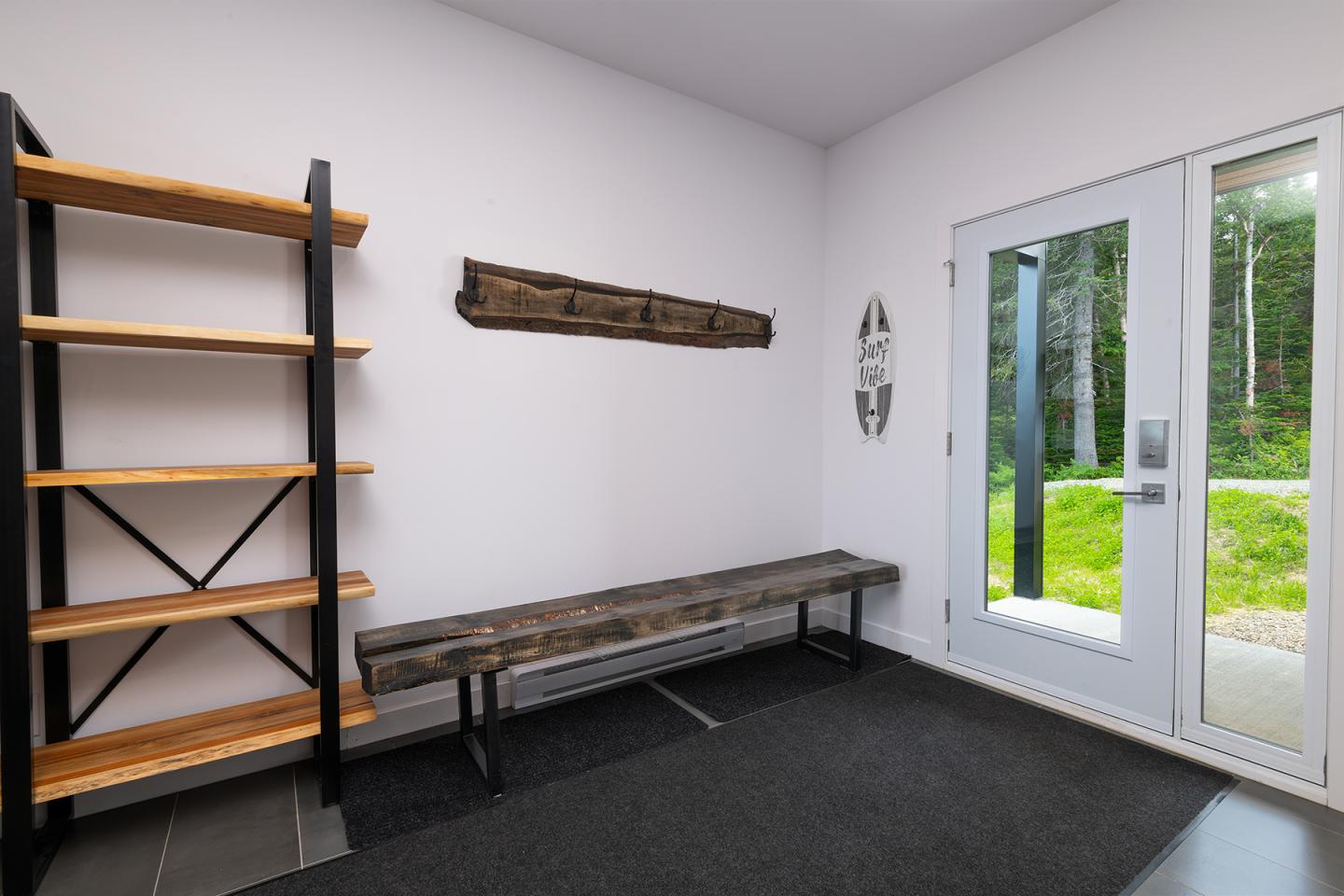 Entrée moderne avec étagère, banc en bois, et porte-fenêtre donnant sur jardin vert.