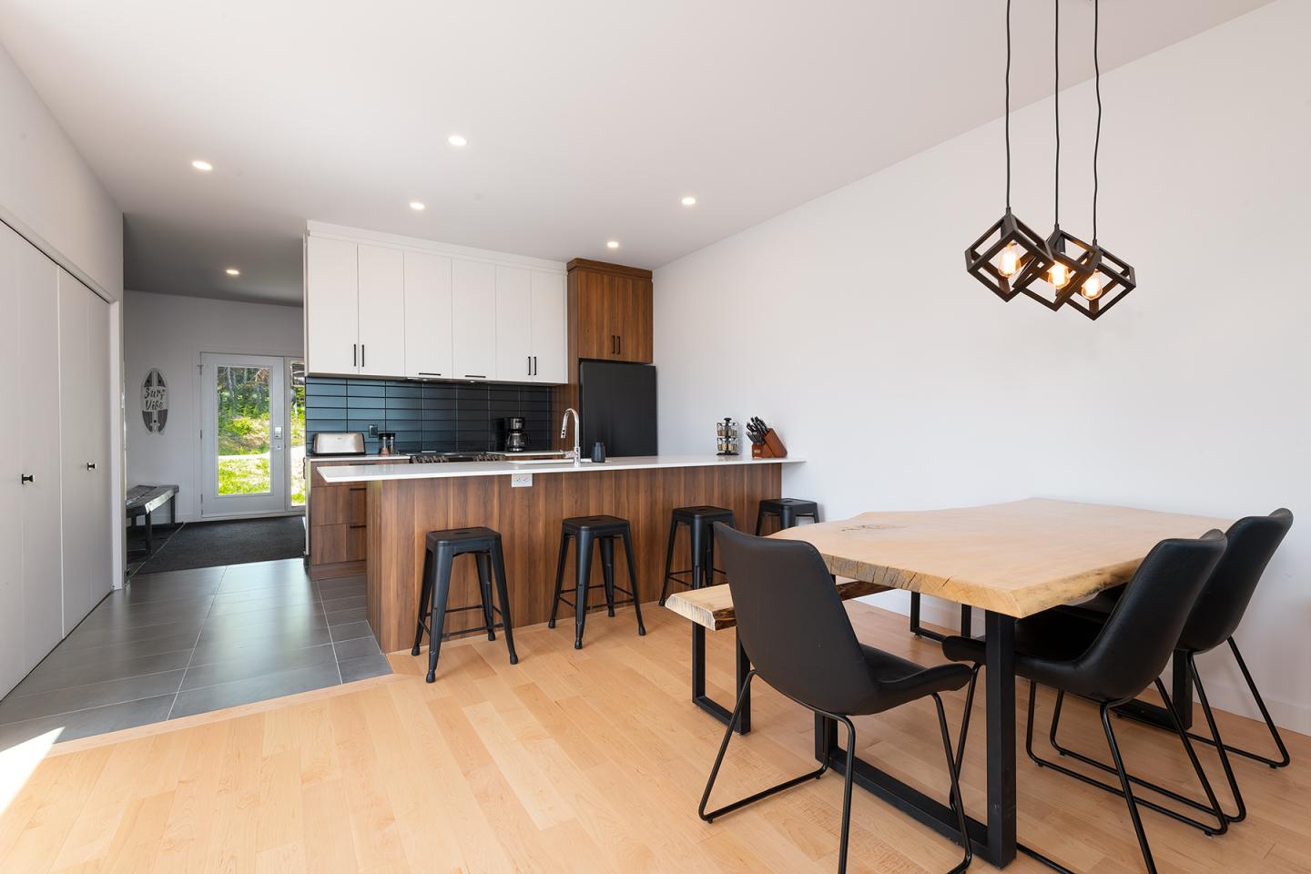 Cuisine moderne avec îlot en bois, chaises noires et table à manger. Lumineuse et épurée.