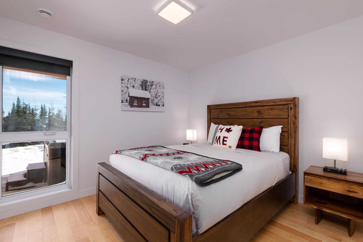 Chambre moderne avec lit en bois, lampes et fenêtre ouverte sur paysage.