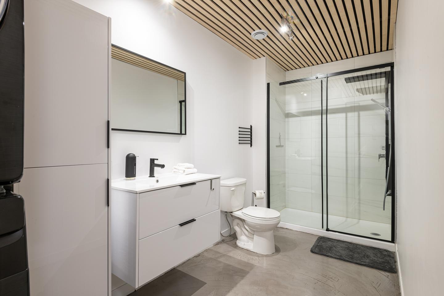 Salle de bain moderne avec douche vitrée, lavabo blanc et plafond en bois.