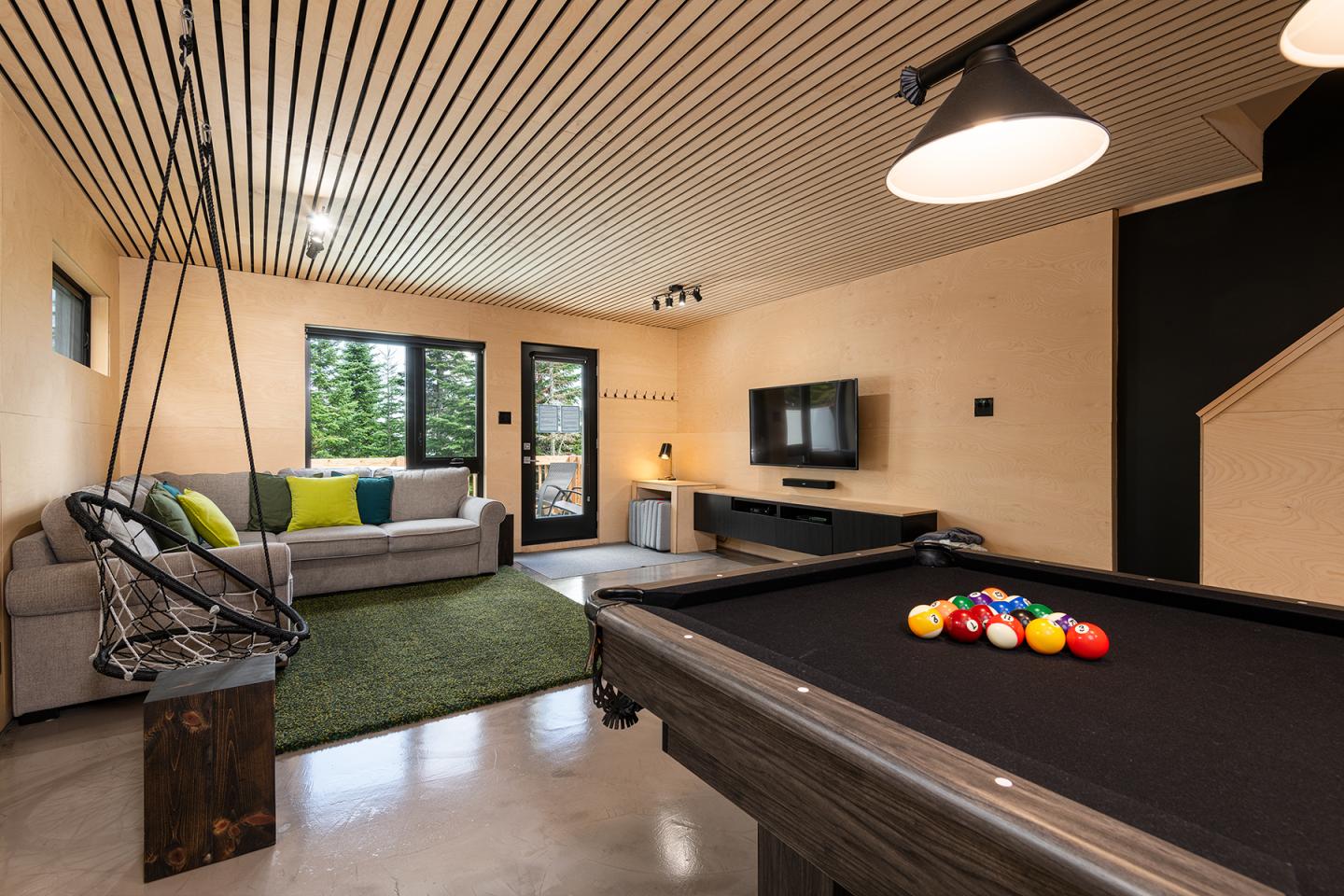 Salon moderne avec table de billard, canapé gris et télé murale.